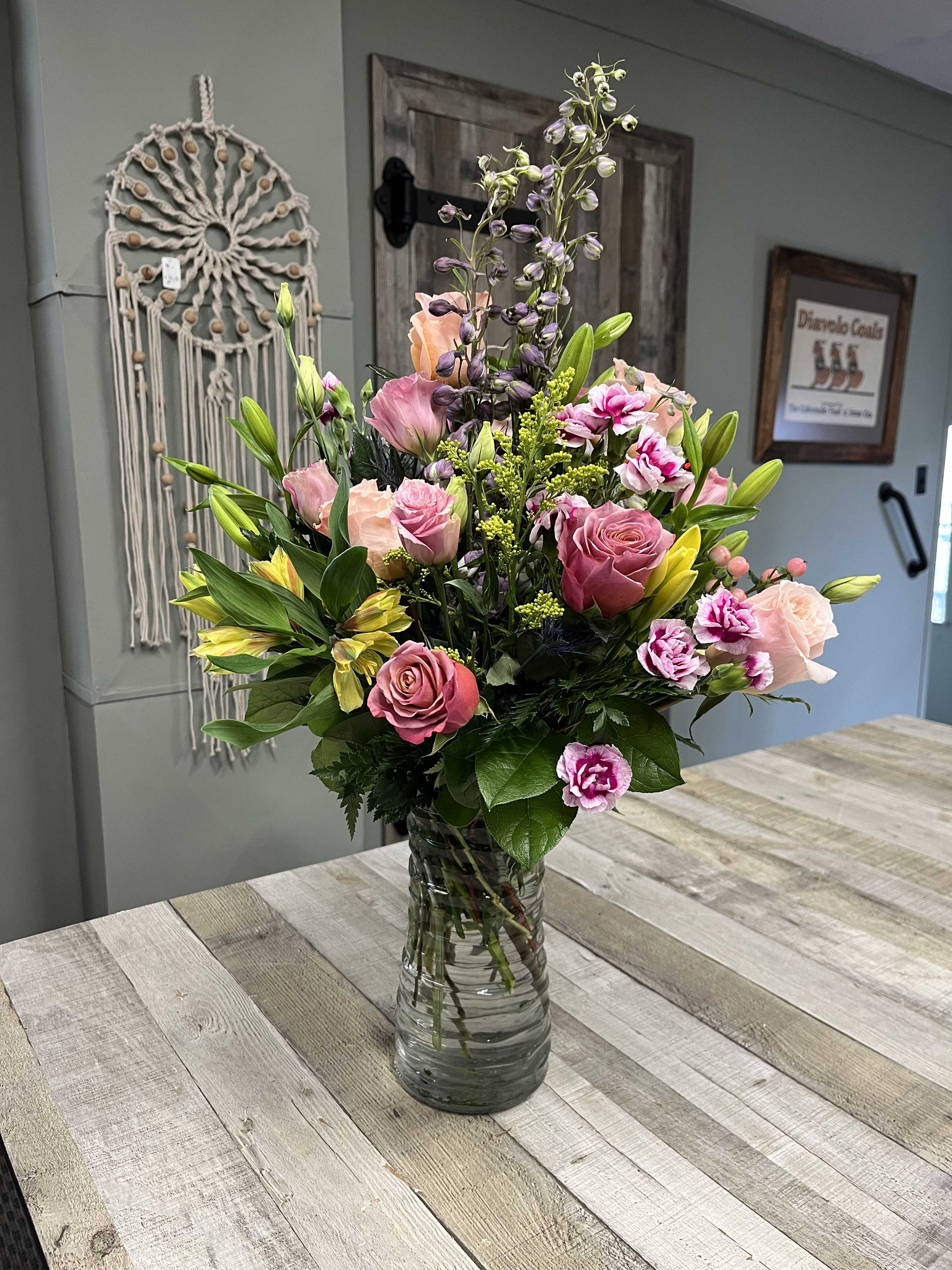 Mixed pink and yellow flowers arranged in a clear glass vase