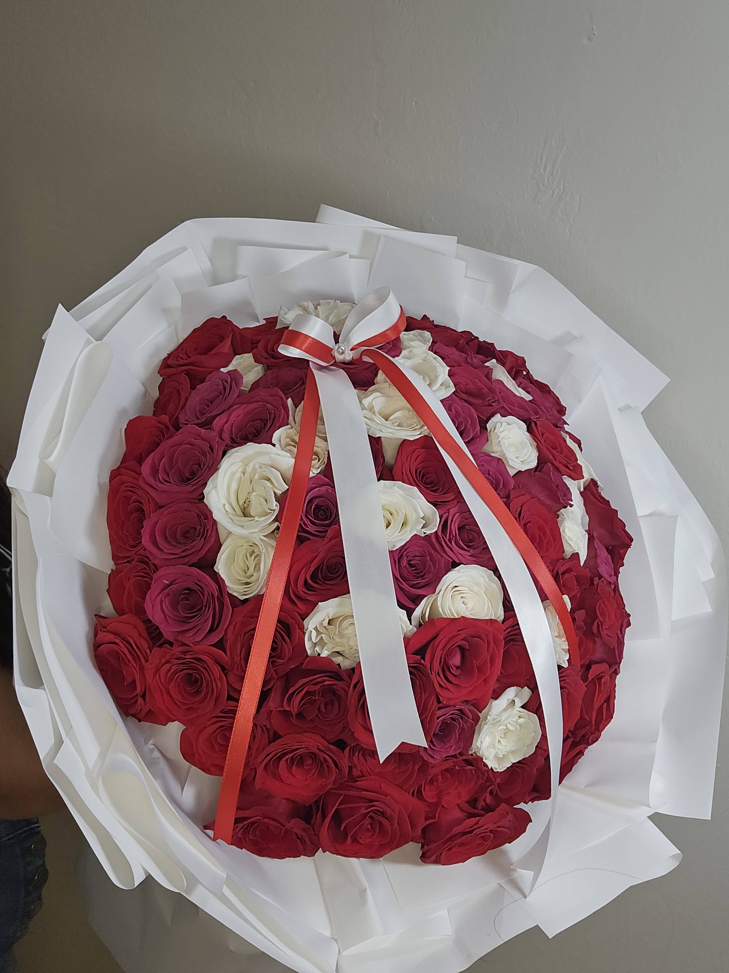 Round bouquet of red and white roses wrapped in white paper with a ribbon