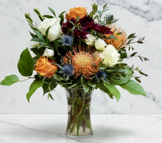 Bouquet of orange, white, and burgundy flowers in a clear glass vase