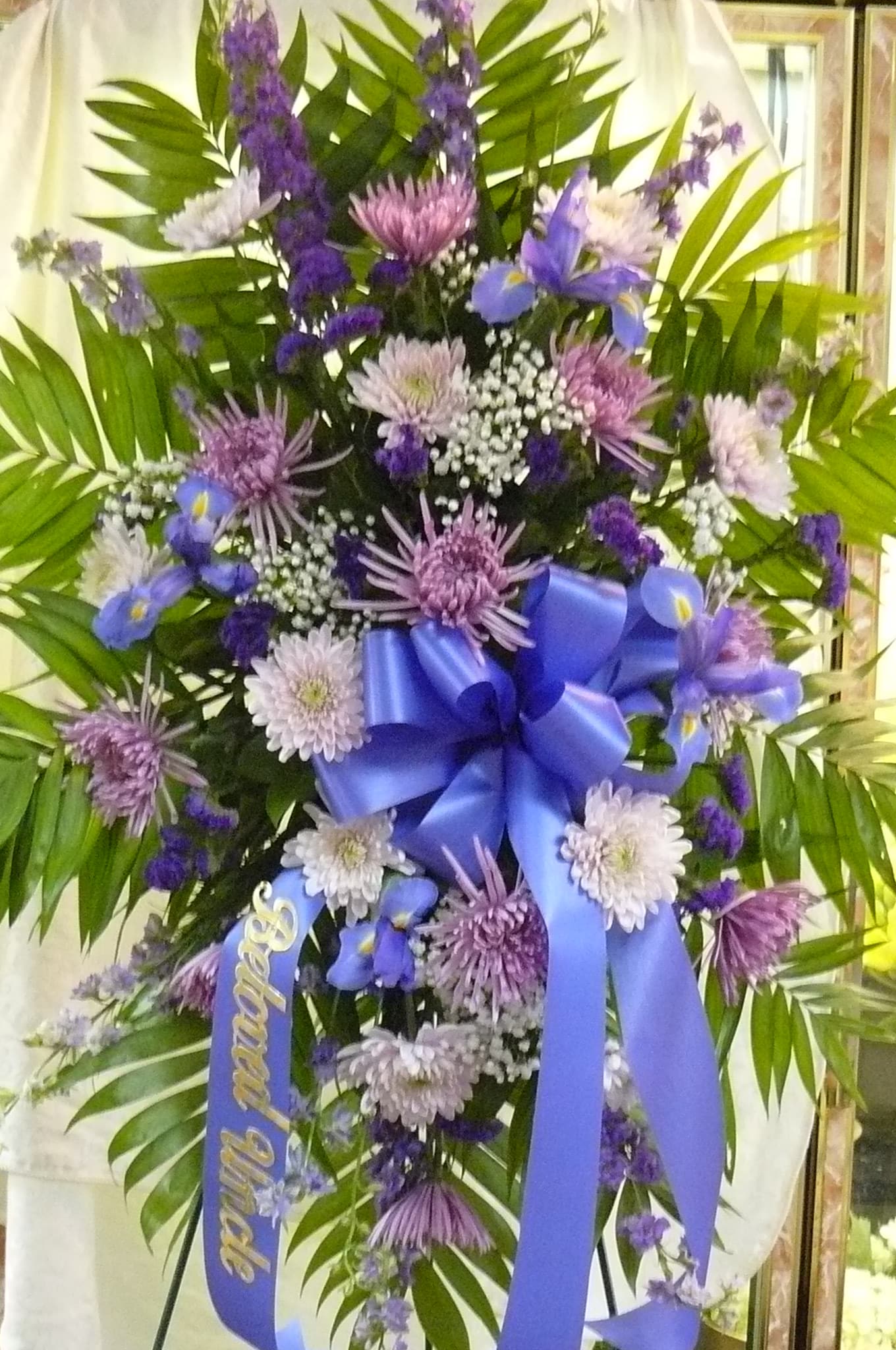 Purple and white funeral spray with a blue ribbon and palm fronds