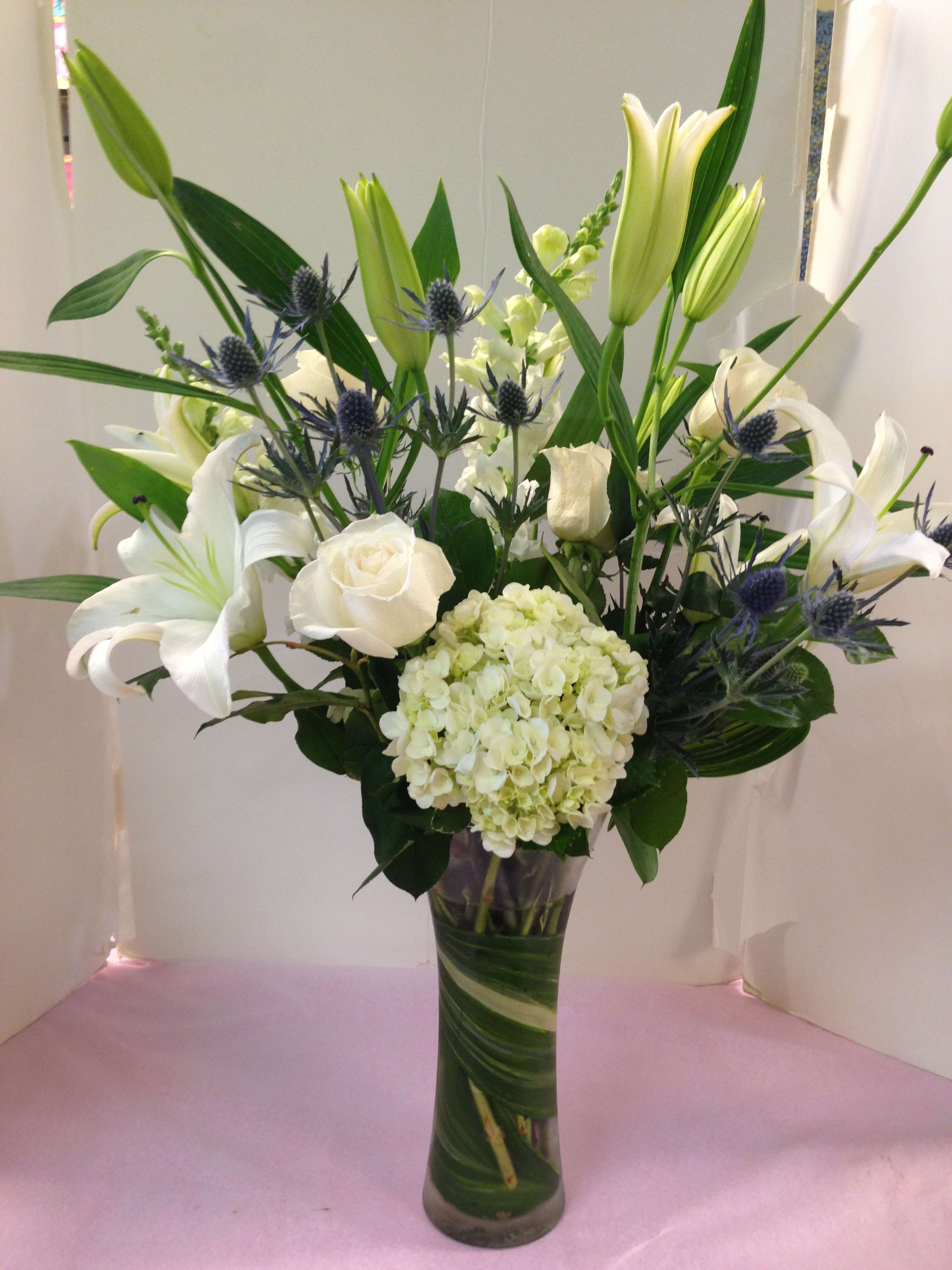 White lilies and roses in a tall glass vase with blue thistle accents