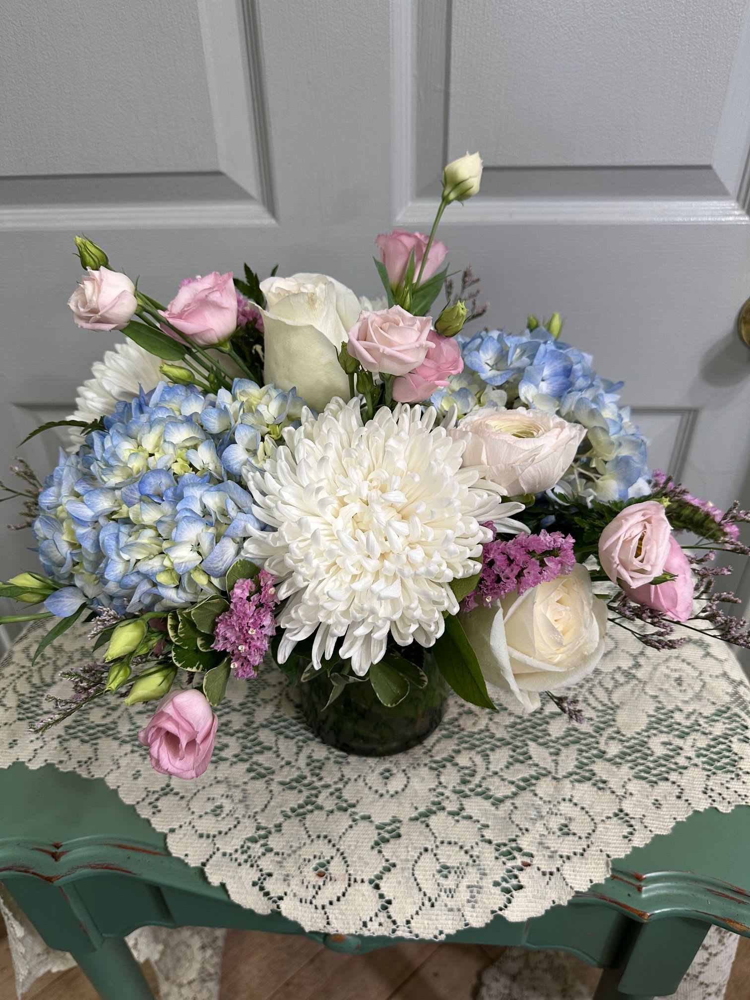 Pastel bouquet with blue hydrangeas, white chrysanthemum, and pink roses in a glass vase.
