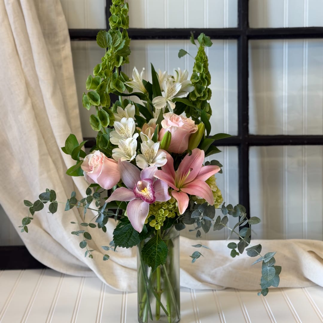 Pink lilies and roses in a glass vase with white flowers and greenery