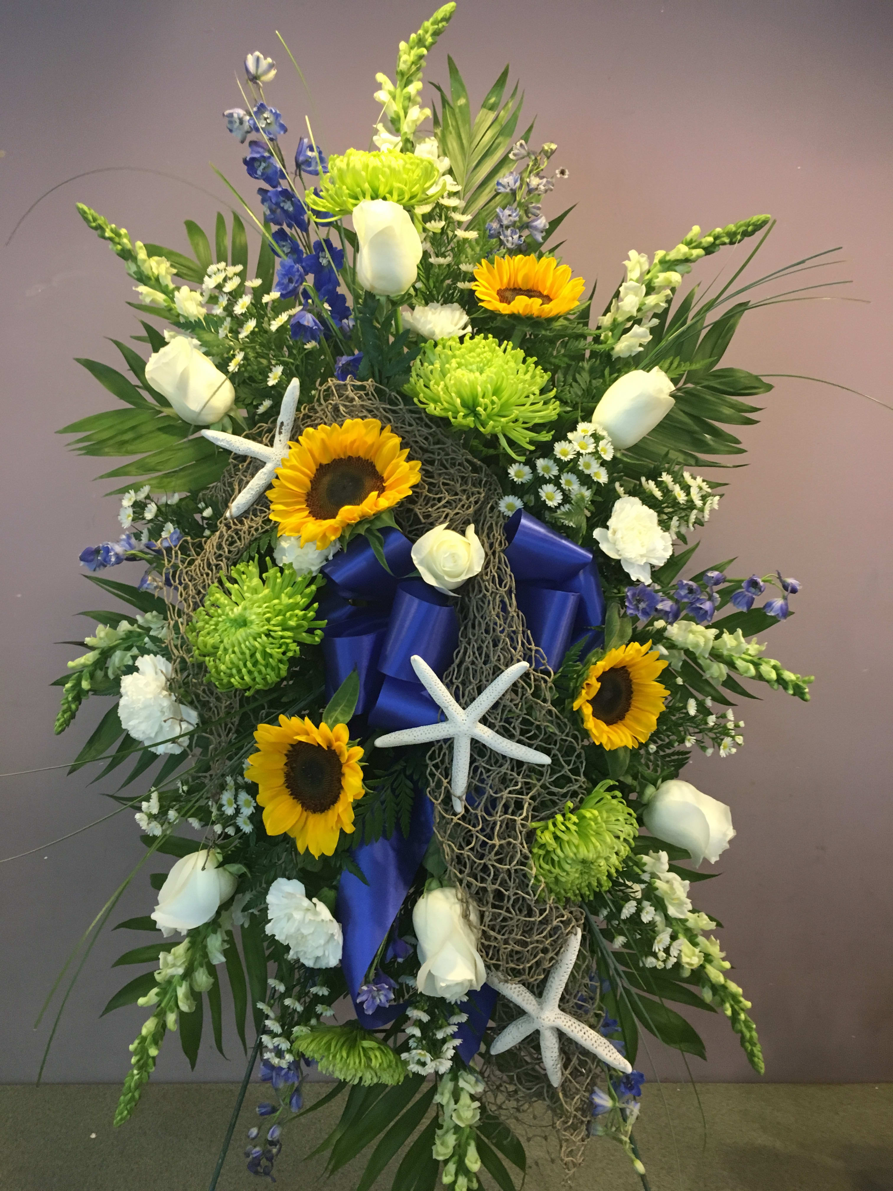 Large floral standing spray with sunflowers, white roses, and blue ribbon