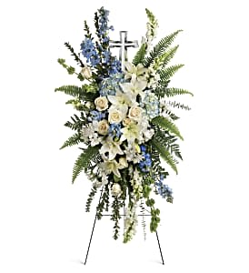 Standing funeral spray with white lilies, blue flowers, and a cross