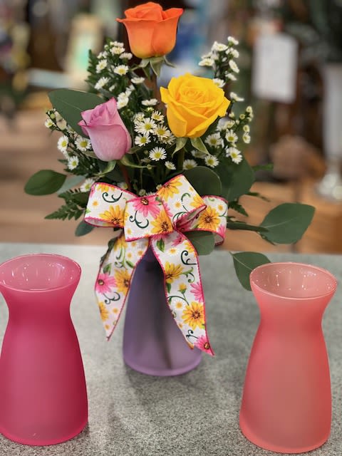 Small bouquet of roses and white filler flowers in a purple vase with a floral bow.