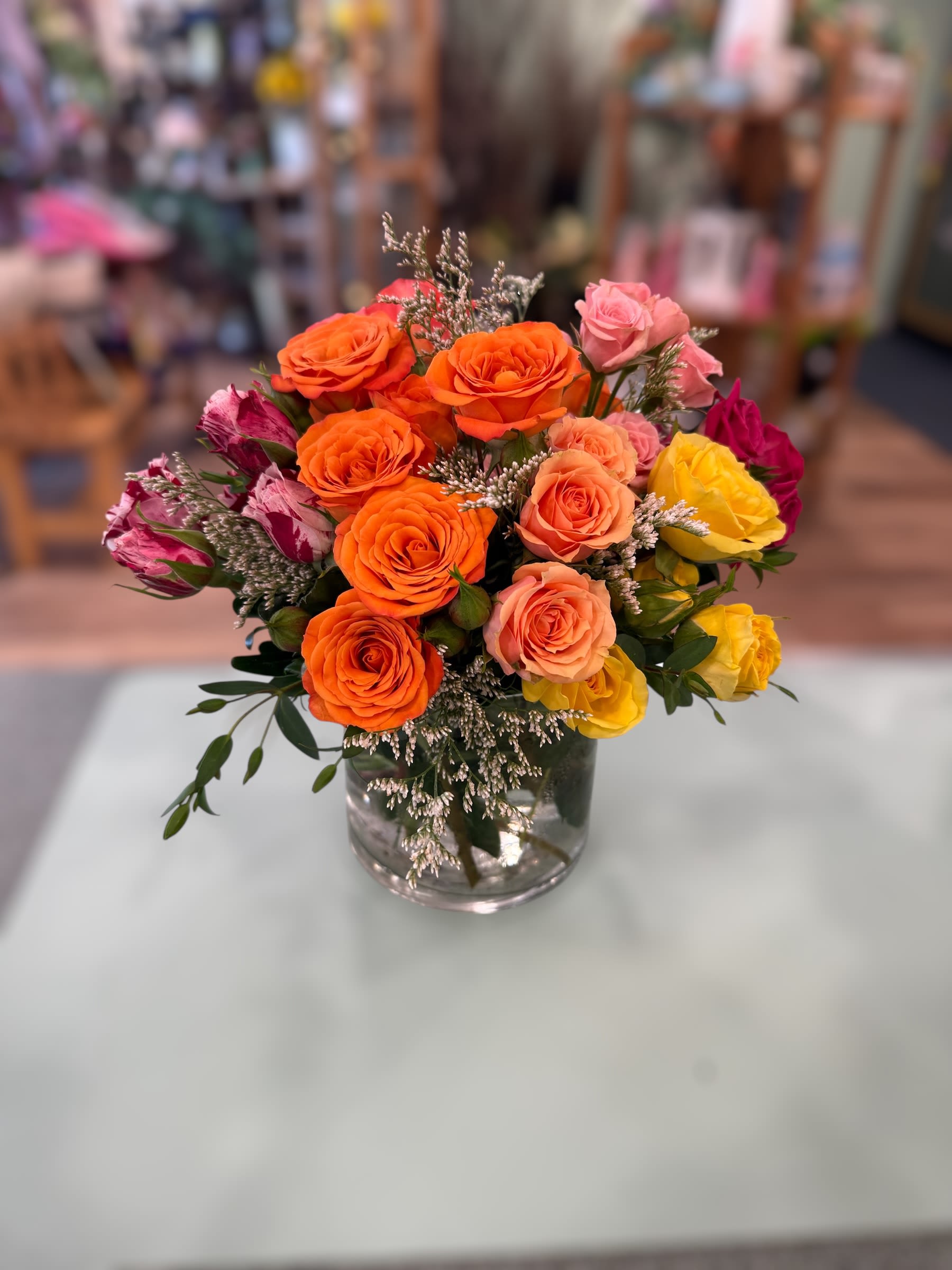 Mixed bouquet of orange, pink, and yellow roses with white filler flowers in a clear glass vase