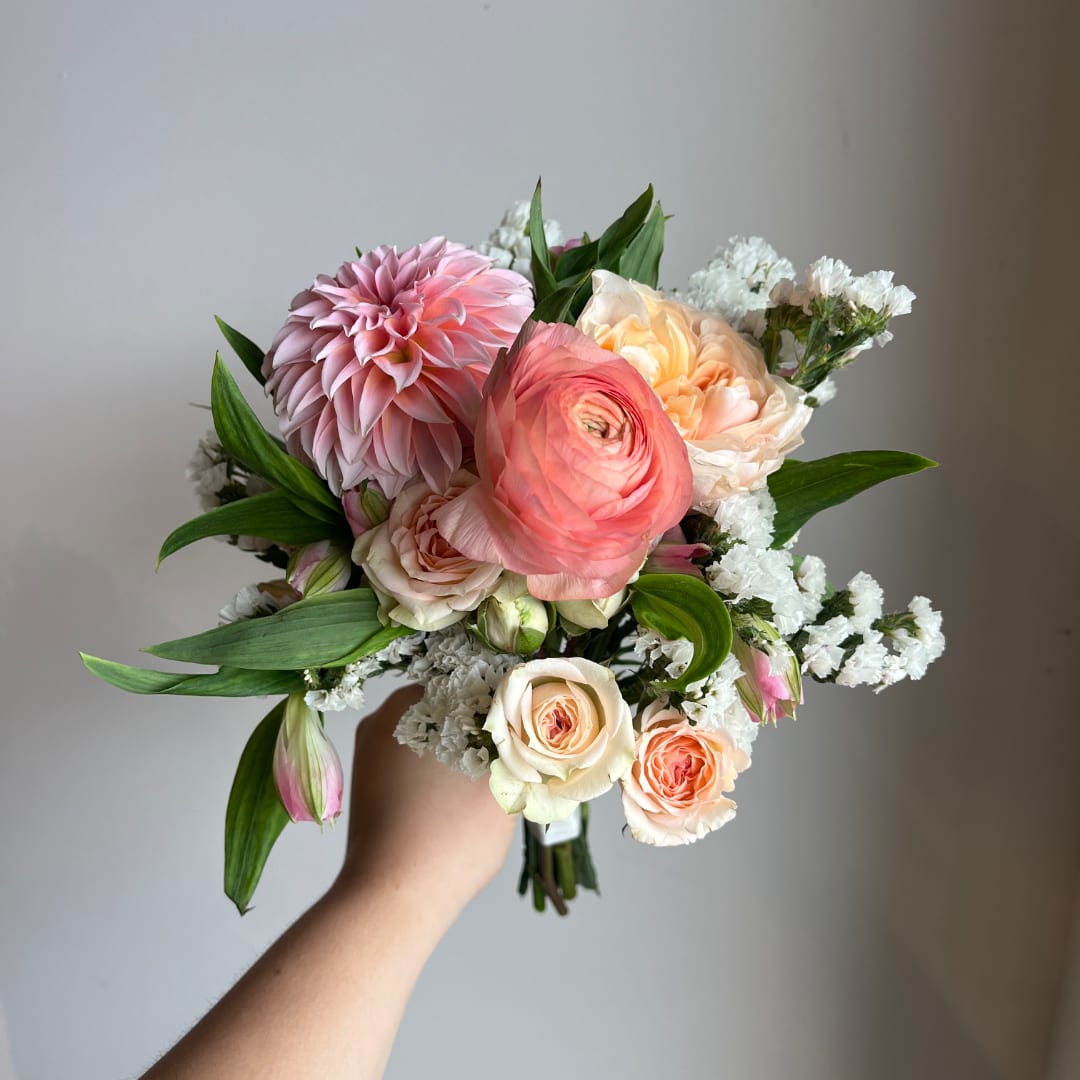 Handheld bouquet with pink and peach flowers and white filler blooms