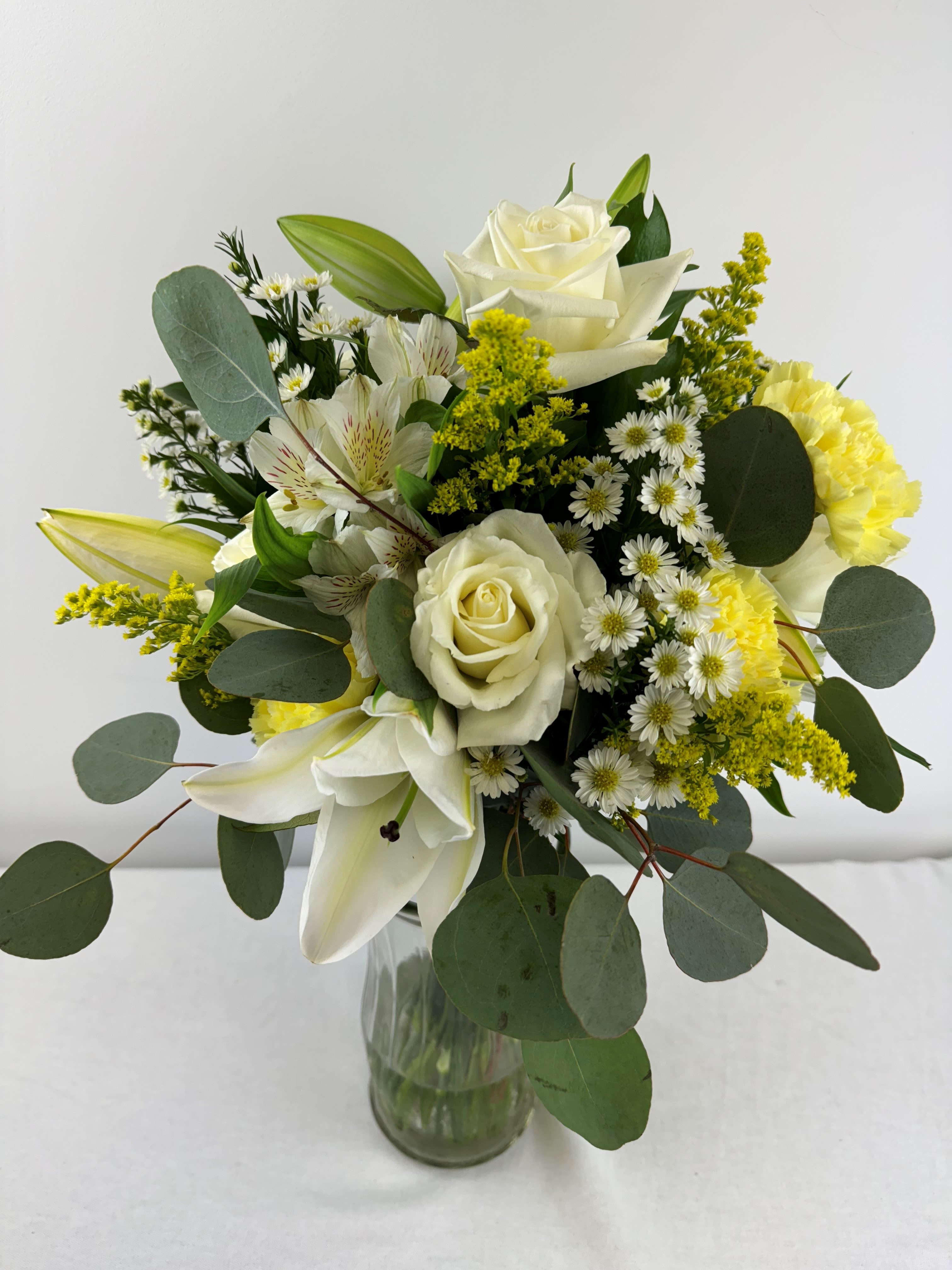 White roses and lilies in a glass vase with yellow filler flowers