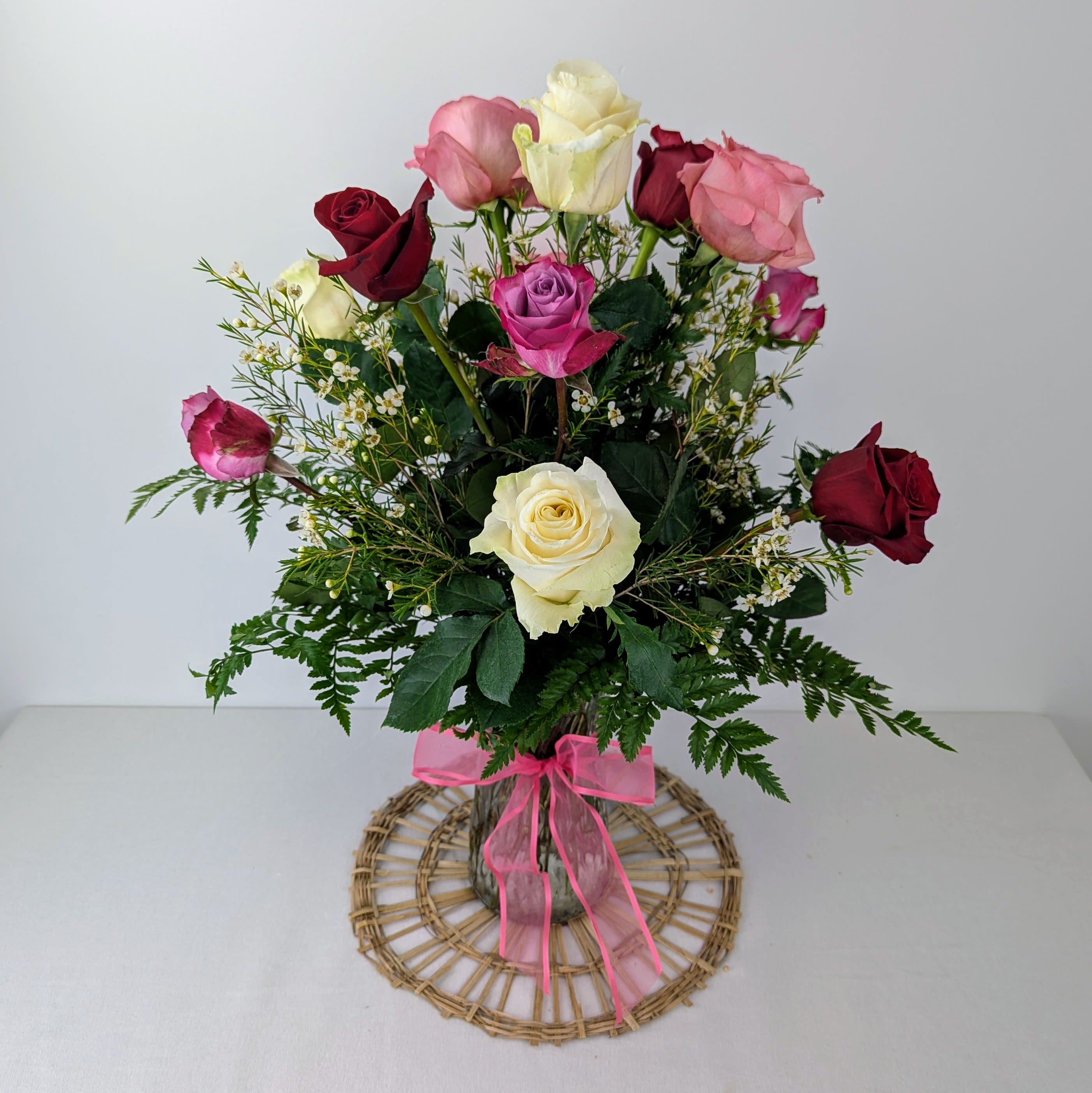 Bouquet of multicolored roses in a clear vase with a pink ribbon