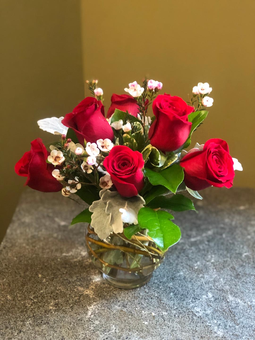 Red roses arranged in a clear glass vase with small white filler flowers.