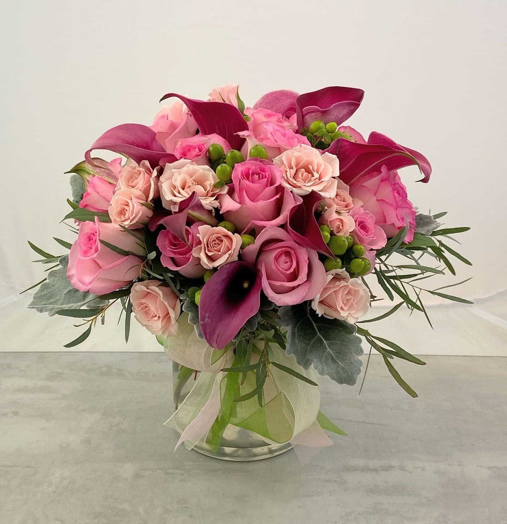Pink and magenta bouquet with roses and calla lilies in a glass vase