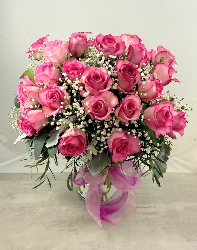 Pink roses arranged in a glass vase with baby's breath and ribbon