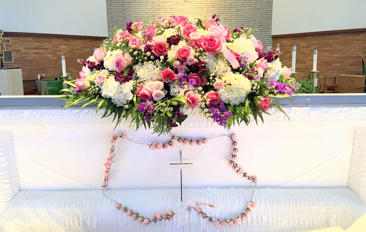 Large pink, white, and purple floral spray on a white casket