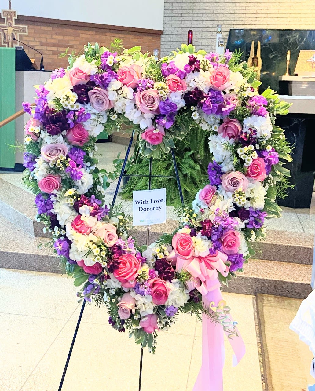 Heart-shaped floral wreath with pink, purple, and white flowers on a stand