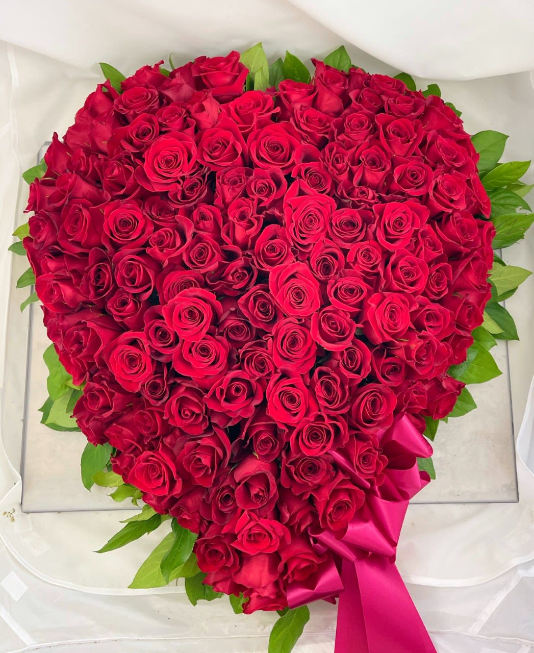 Heart-shaped bouquet of red roses with a pink ribbon