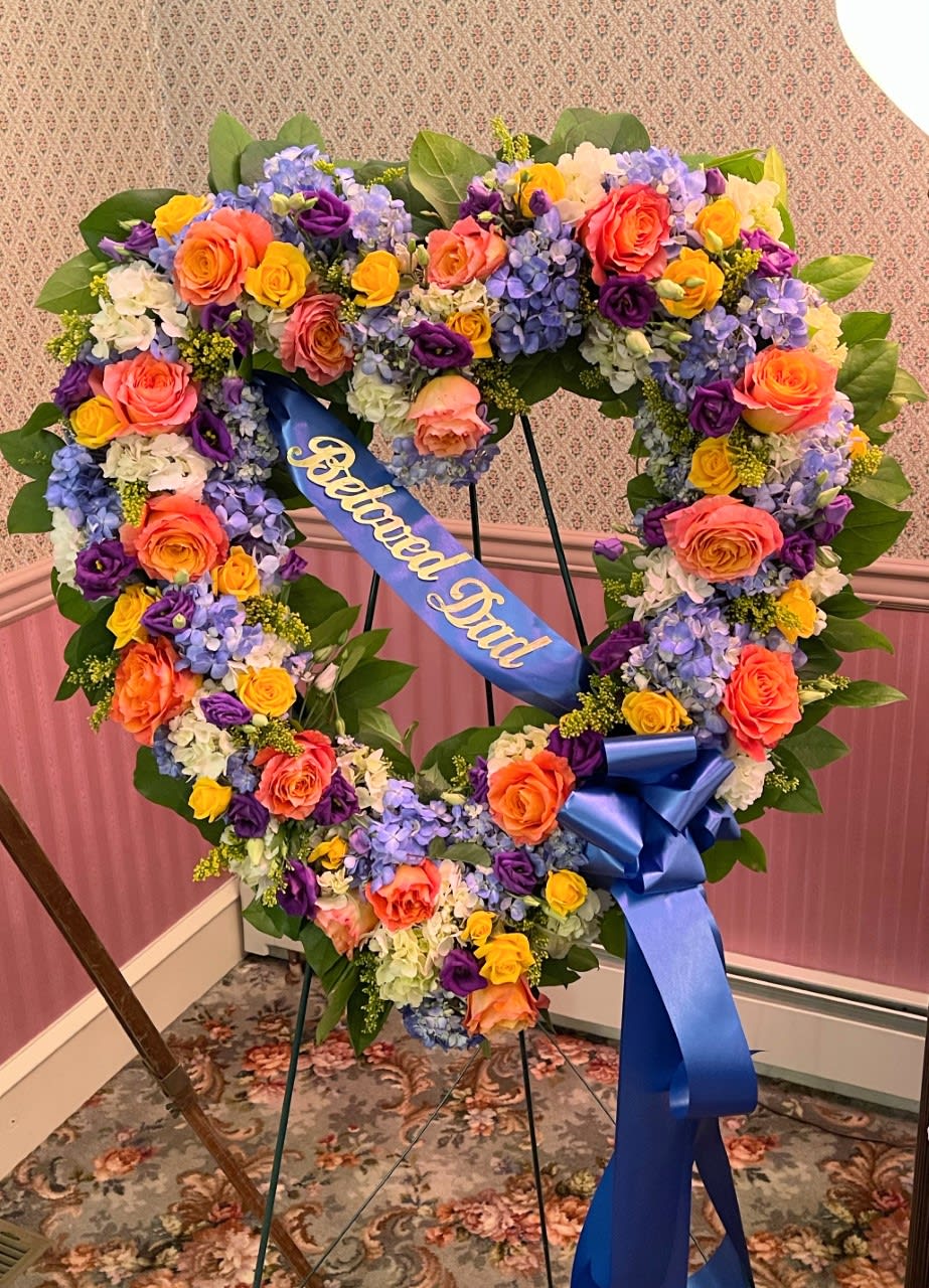 Heart-shaped floral wreath with a blue memorial ribbon on a stand