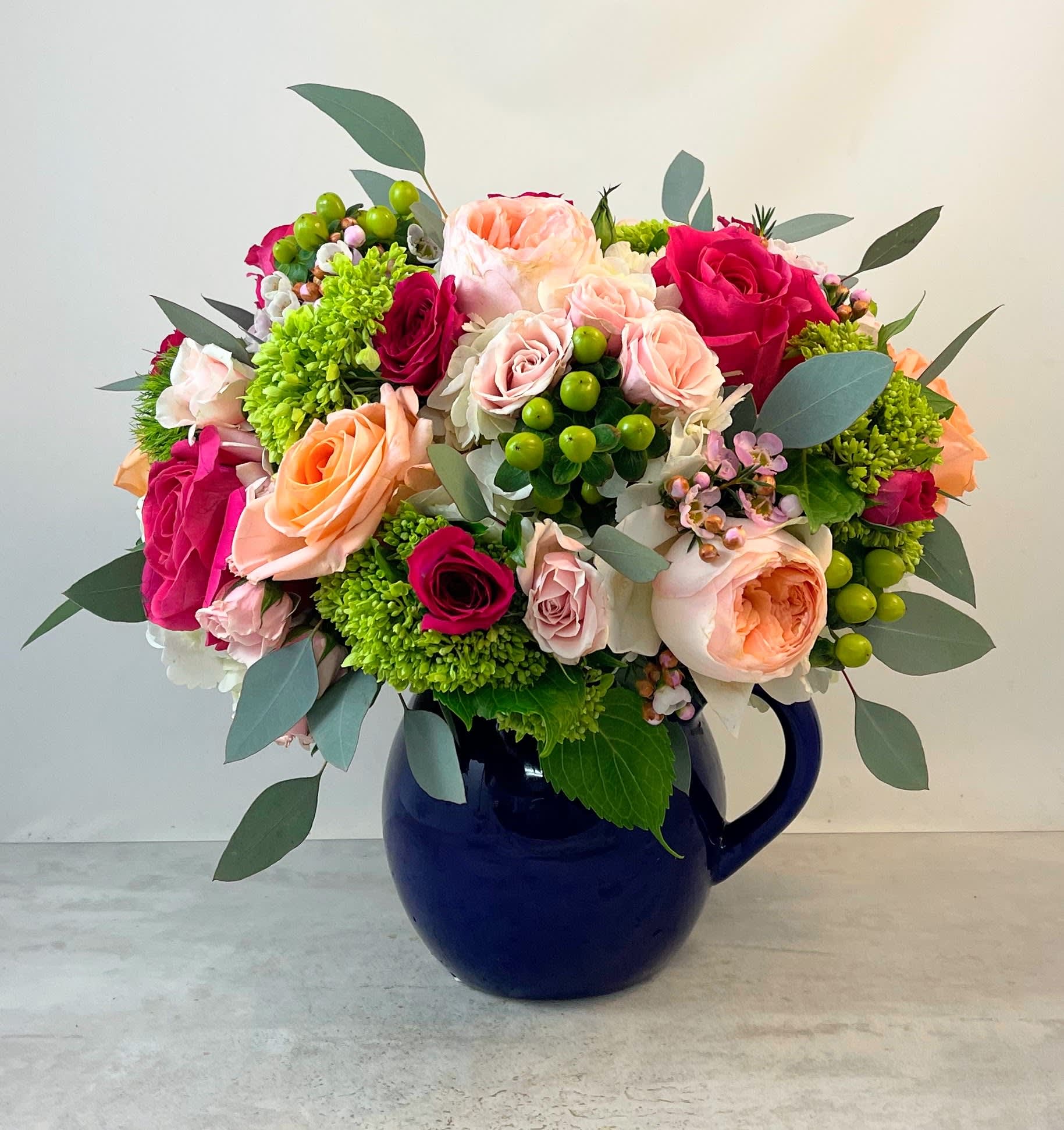 Mixed bouquet of pink, peach, and green flowers in a blue pitcher vase