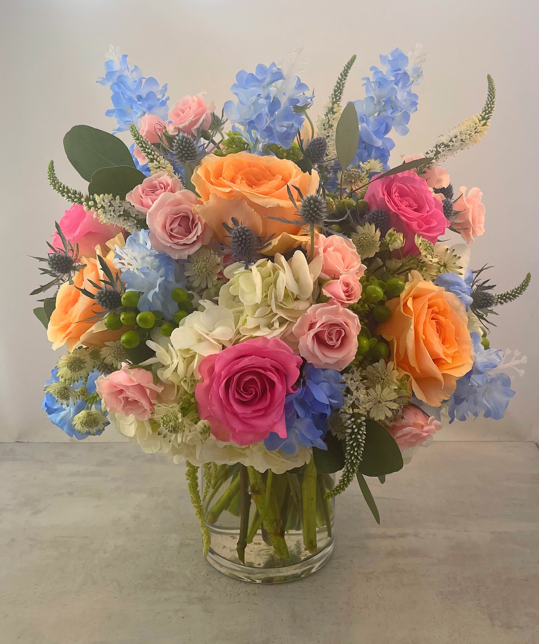Mixed bouquet of roses, hydrangeas, and blue flowers in a clear glass vase