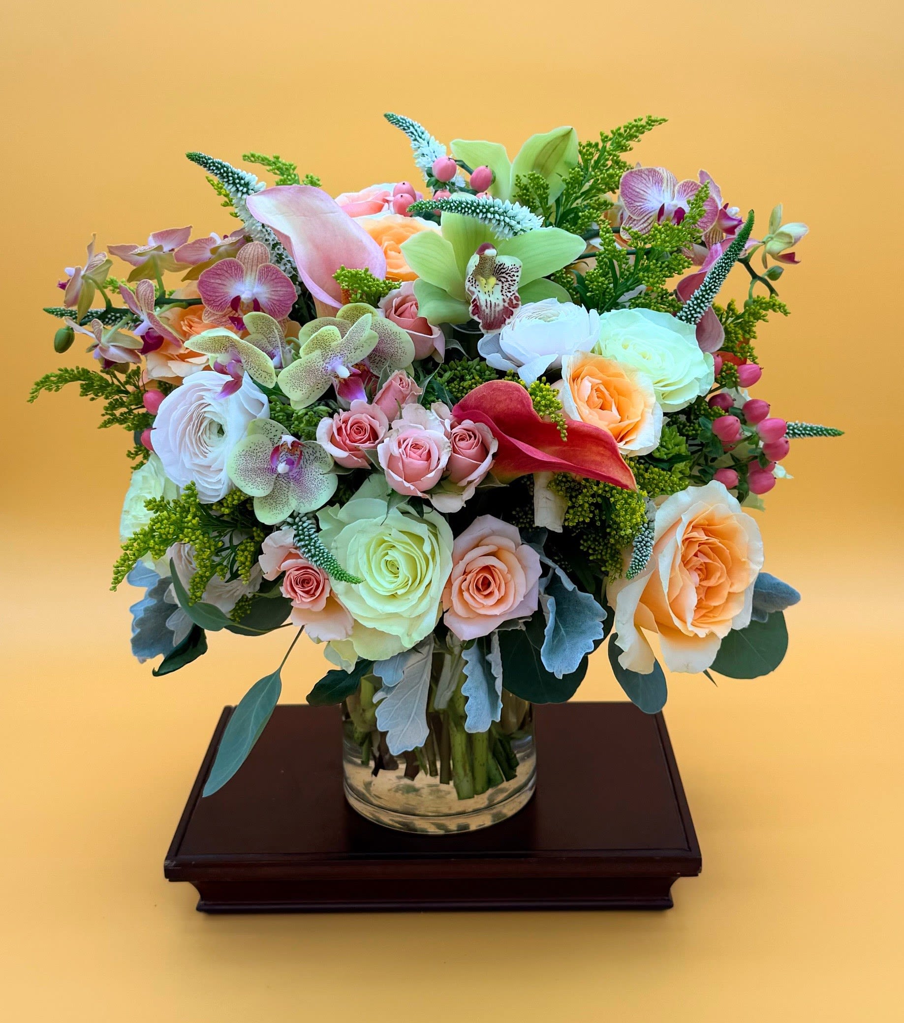 Mixed bouquet of roses, orchids, and calla lilies in a glass vase