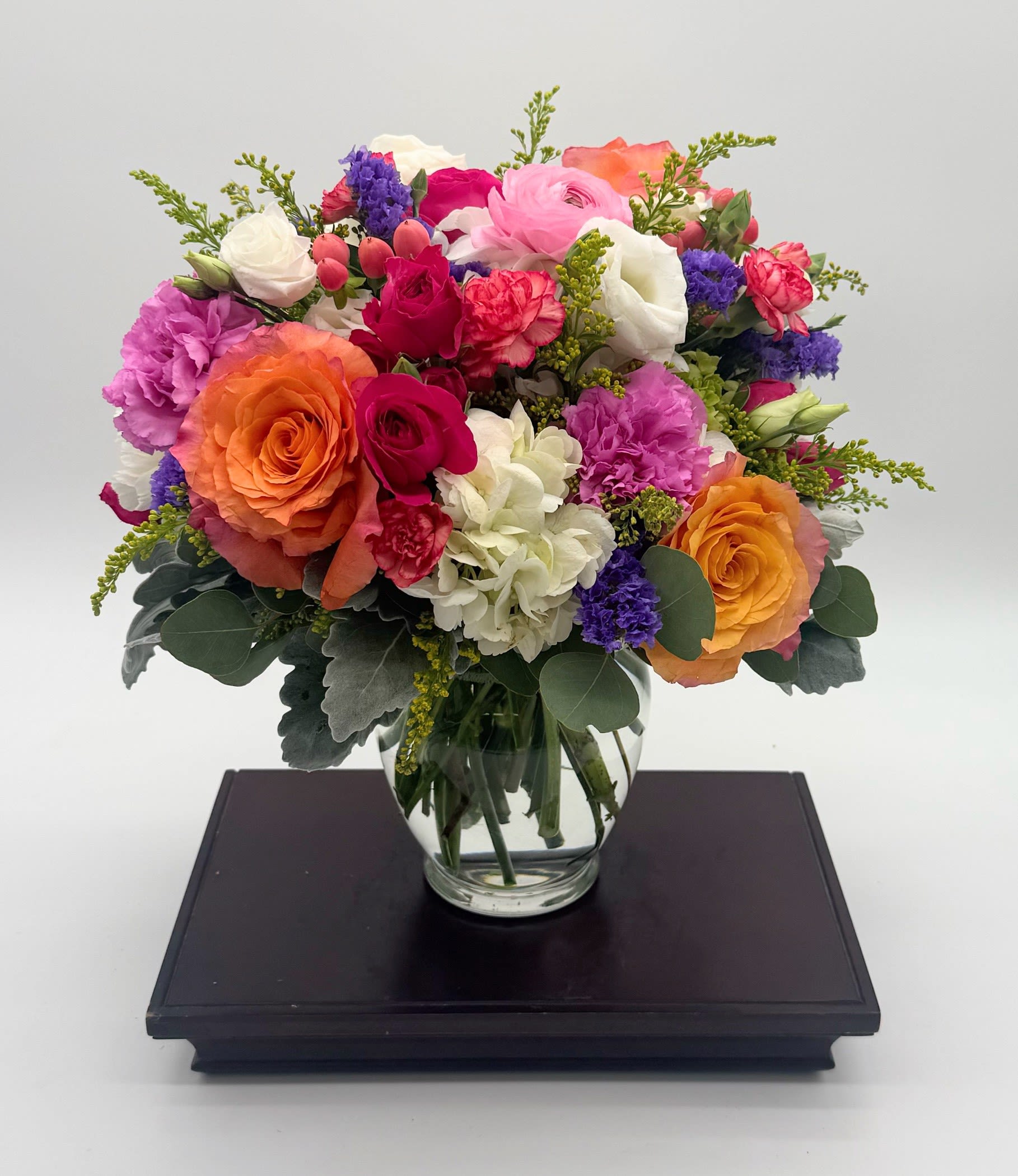 Bright mixed bouquet of roses, carnations, and hydrangeas in a round clear glass vase