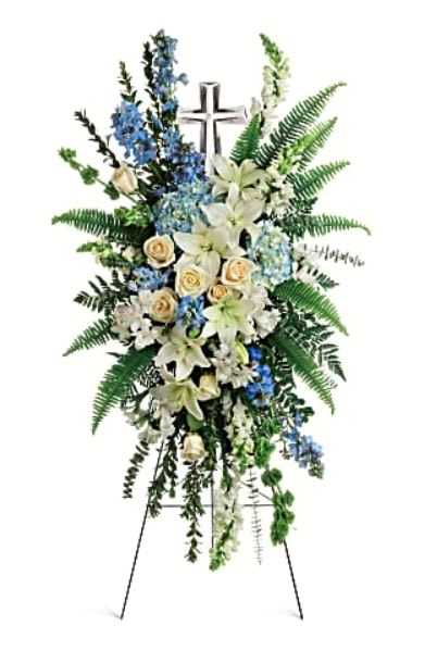 Eternal Grace - Celebrate the eternal grace of a life well lived with this dramatic spray of peaceful white and blue blooms, crowned with a large crystal cross keepsake. •This serene spray includes blue hydrangea,crème roses, white asiatic lilies, white alstroemeria, bells of Ireland, blue delphinium, white snapdragons, myrtle, sword fern, leatherleaf fern, spiral eucalyptus, and variegated pittorsporum.  •Delivered on a wire easel with Teleflora's Large Crystal Cross Keepsake. •Orientation: One-Sided 