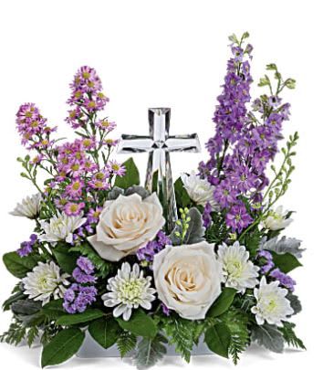 Poised with Love - This beautiful piece includes crème roses, lavender larkspur, lavender montecasino asters, white cushion spray chrysanthemums, lavender sinuata statice, lemon leaf and dusty miller. Delivered with Teleflora's Small Crystal Cross. While supplies last. Approximately 16" W x 16" H