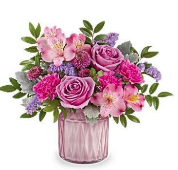 Enchanted Oasis - Experience timeless elegance with Teleflora's Dazzling Gem jar, featuring a radiant pink pearlescent shimmer that perfectly enhances a lush bouquet of pink and purple blooms, bringing artistic charm to any space. Teleflora's Enchanted Oasis Bouquet showcases a stunning mix of lavender roses, pink alstroemeria, fuchsia carnations, purple button spray chrysanthemums, lavender sinuata statice, dusty miller, and huckleberry. Arranged in a pink pearlescent vase, this elegant bouquet adds a touch of timeless charm to any space.
