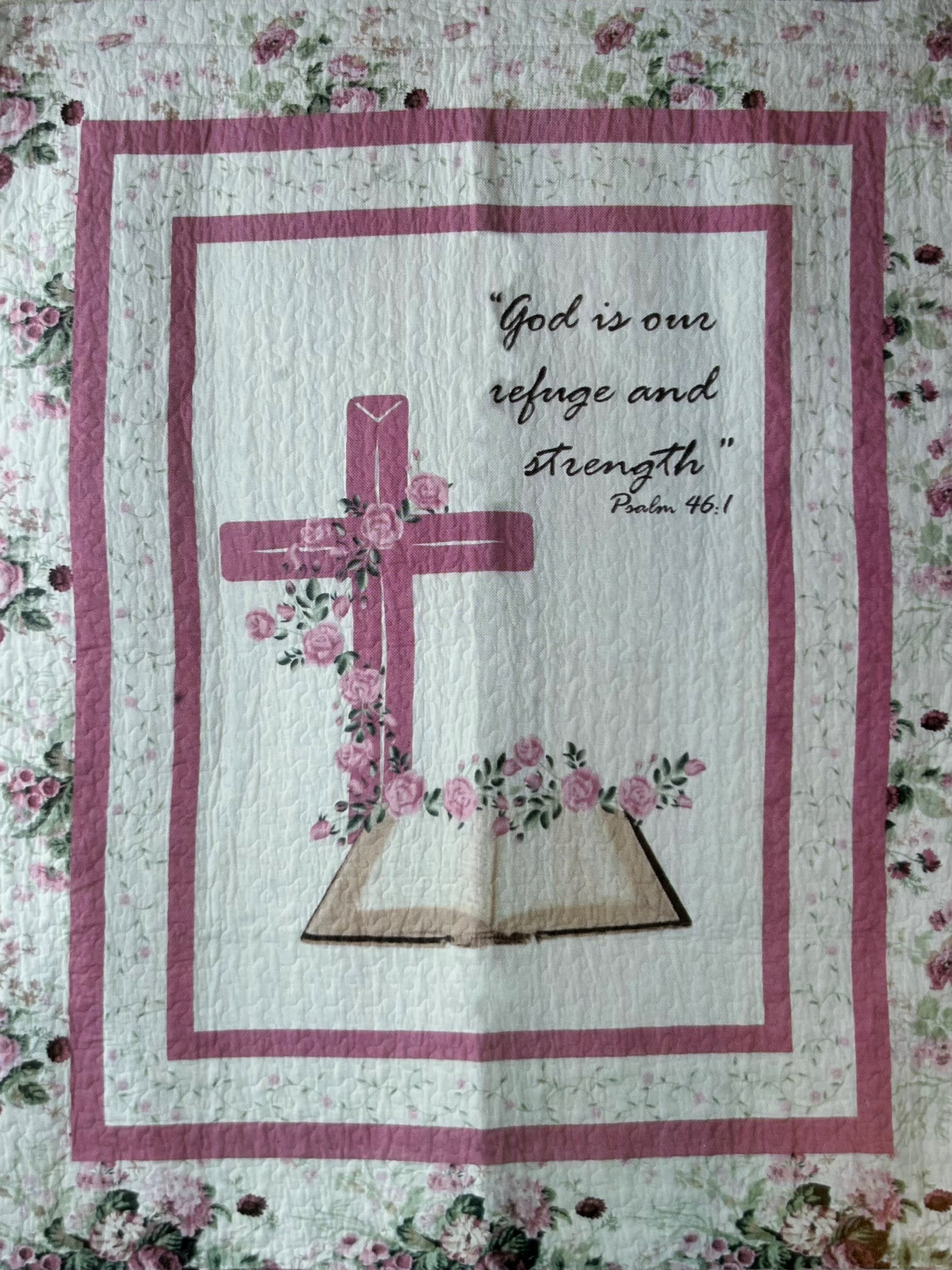 Psalm 46:1 God is our refuge and strength Quilted Throw - A soft, devotional keepsake that comforts at difficult times, this Psalm 46:1 quilted throw pairs a centered pink cross and delicate rose clusters with the reassuring words "God is our refuge and strength" printed in black script-perfect as a sympathy or funeral gift and also thoughtful for a get-well gesture. The feminine patchwork look and floral border prints create a handmade, homey feel that will offer quiet solace when draped over a chair or folded at the foot of a bed.  Made from 100% cotton and measuring 50" x 60", the quilt features white panels, pink accents, and black lettering for clear, gentle contrast; it arrives ready to display or tuck into a care package. For memorial services or a more formal presentation, add the metal easel stand (available as an upgrade) to hold the quilt or a tribute sign upright-an easy way to honor a loved one and create a comforting focal point in the room.