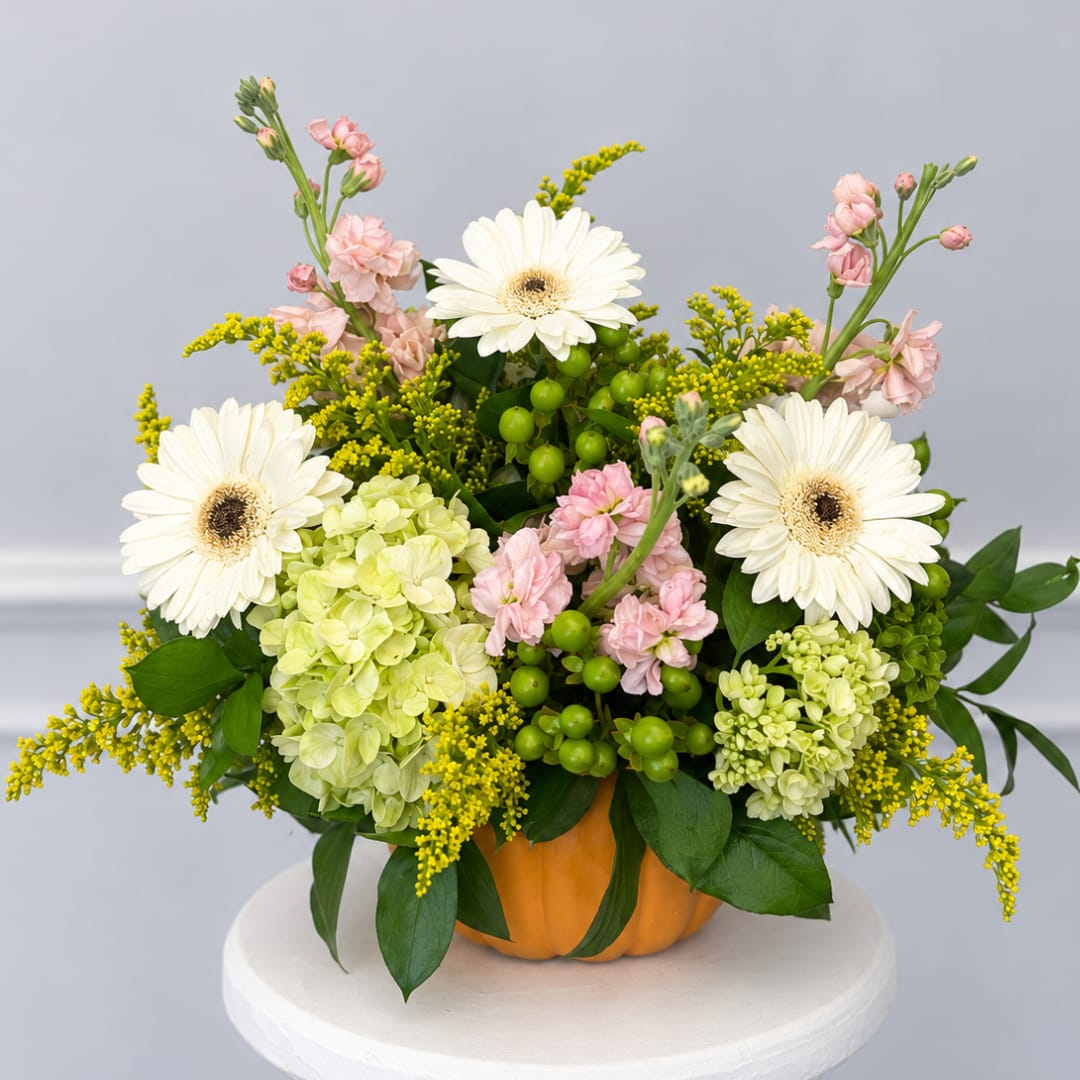 Flower arrangement in a pumpkin container with white daisies and pink blooms