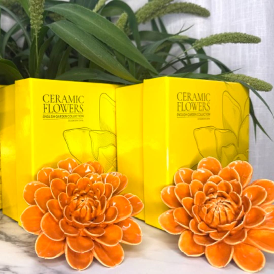 Two orange ceramic flowers in yellow boxes with green foliage behind