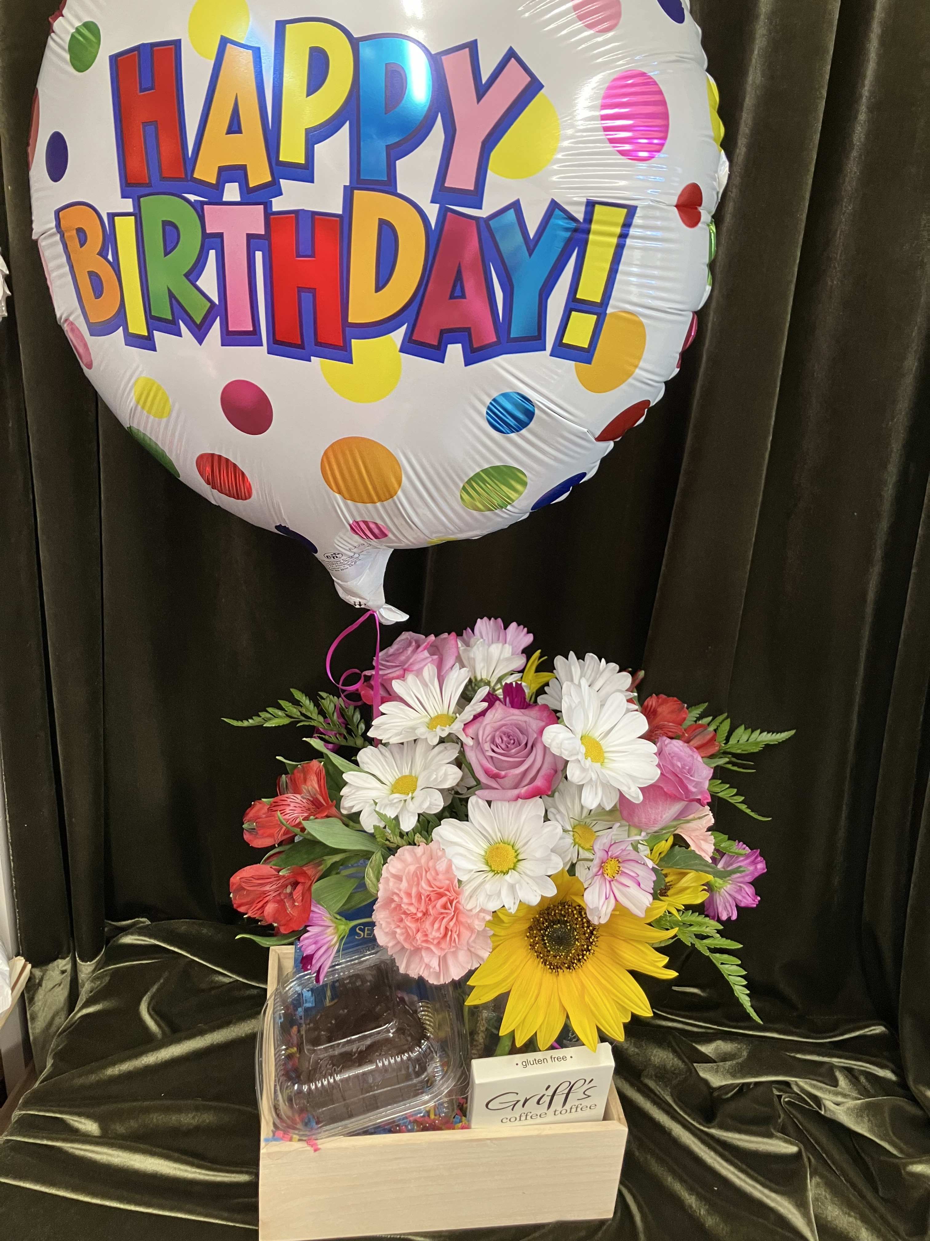 Birthday balloon above a mixed flower arrangement in a wooden box with chocolates