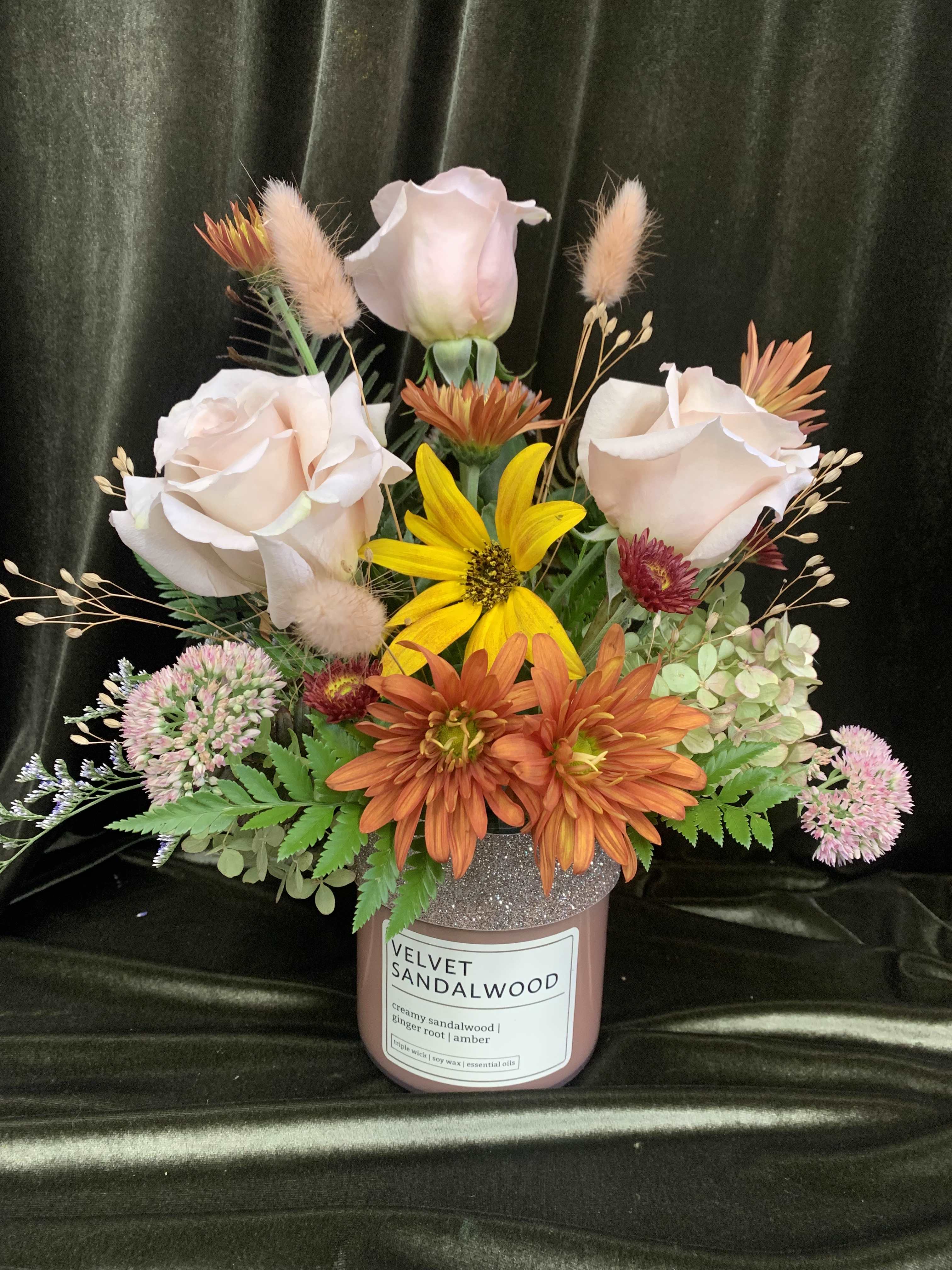 Mixed floral arrangement in a pink candle jar with pale roses and orange daisies