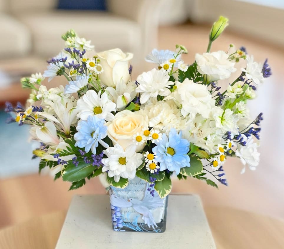 White and blue mixed bouquet in a square glass vase