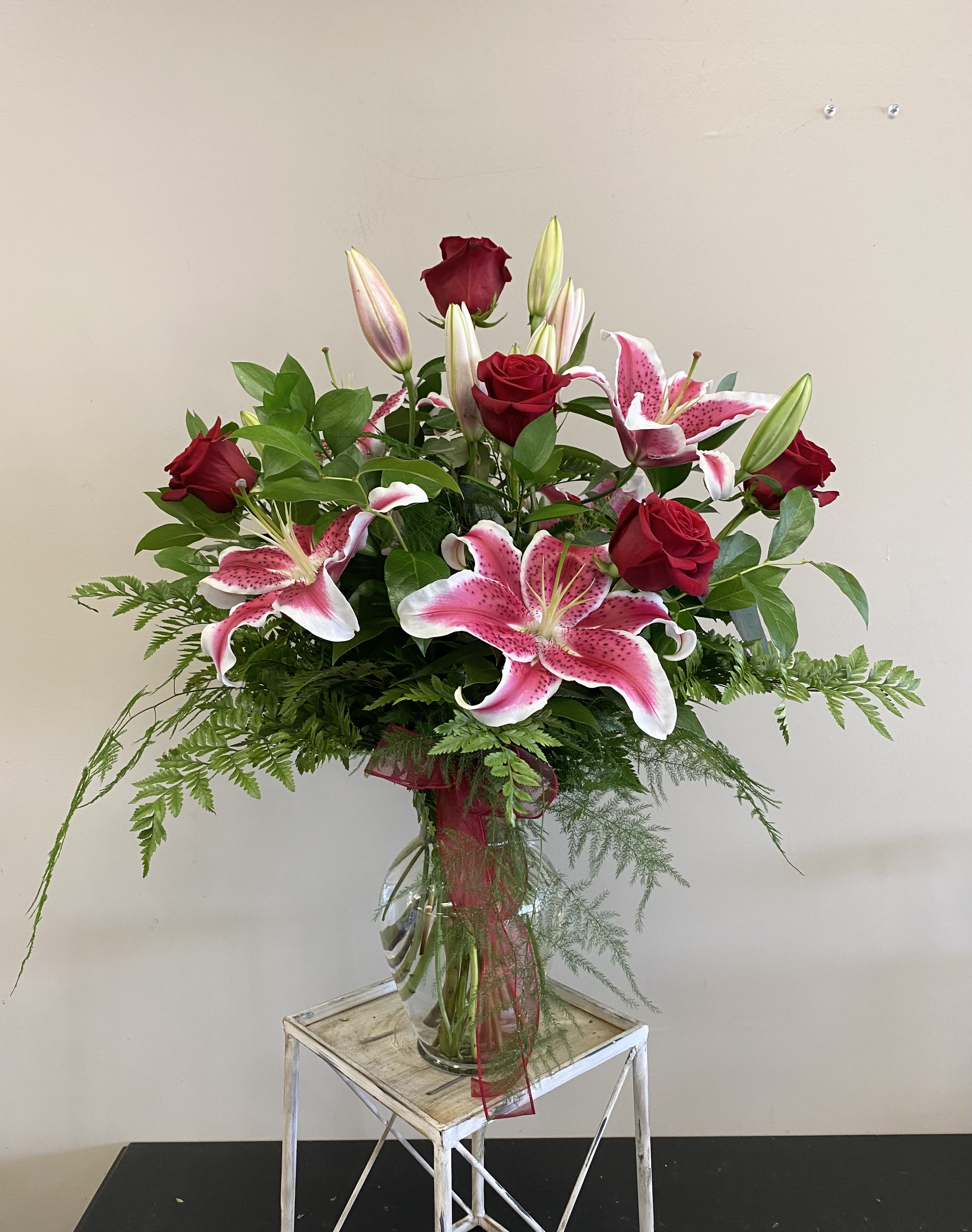 Tall vase arrangement of red roses and pink lilies with a red ribbon bow.