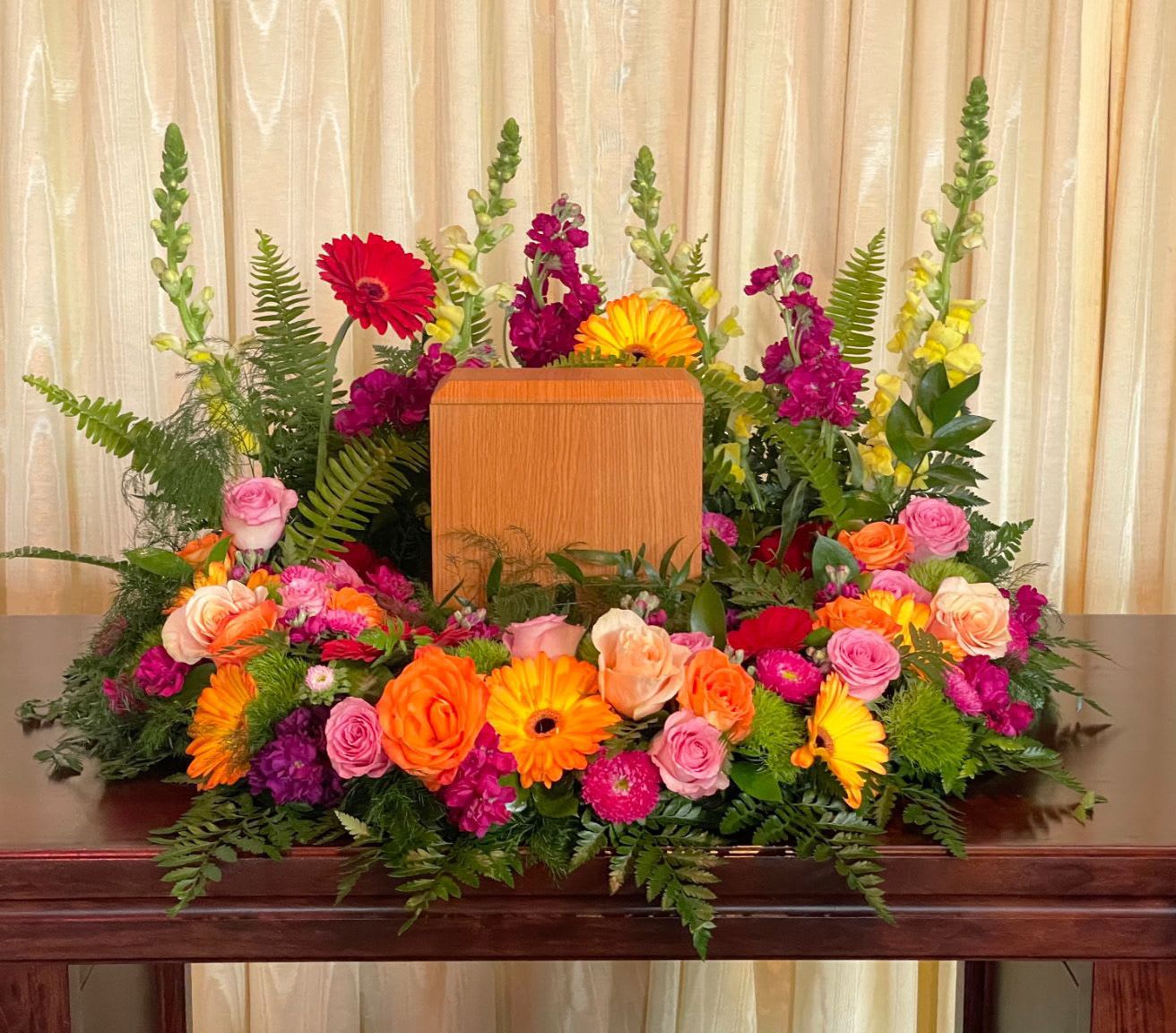 Colorful floral arrangement surrounding a wooden urn on a table
