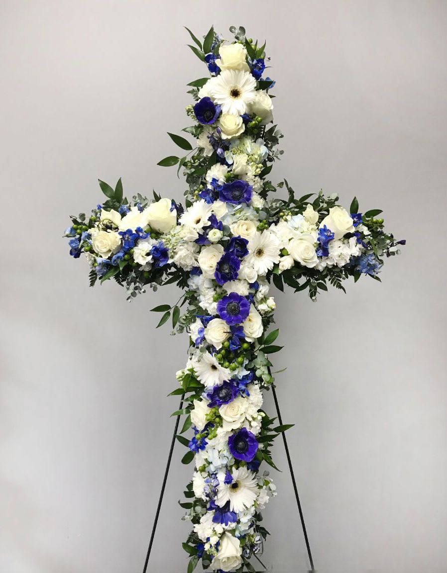 Standing floral cross of white and blue flowers on a metal easel