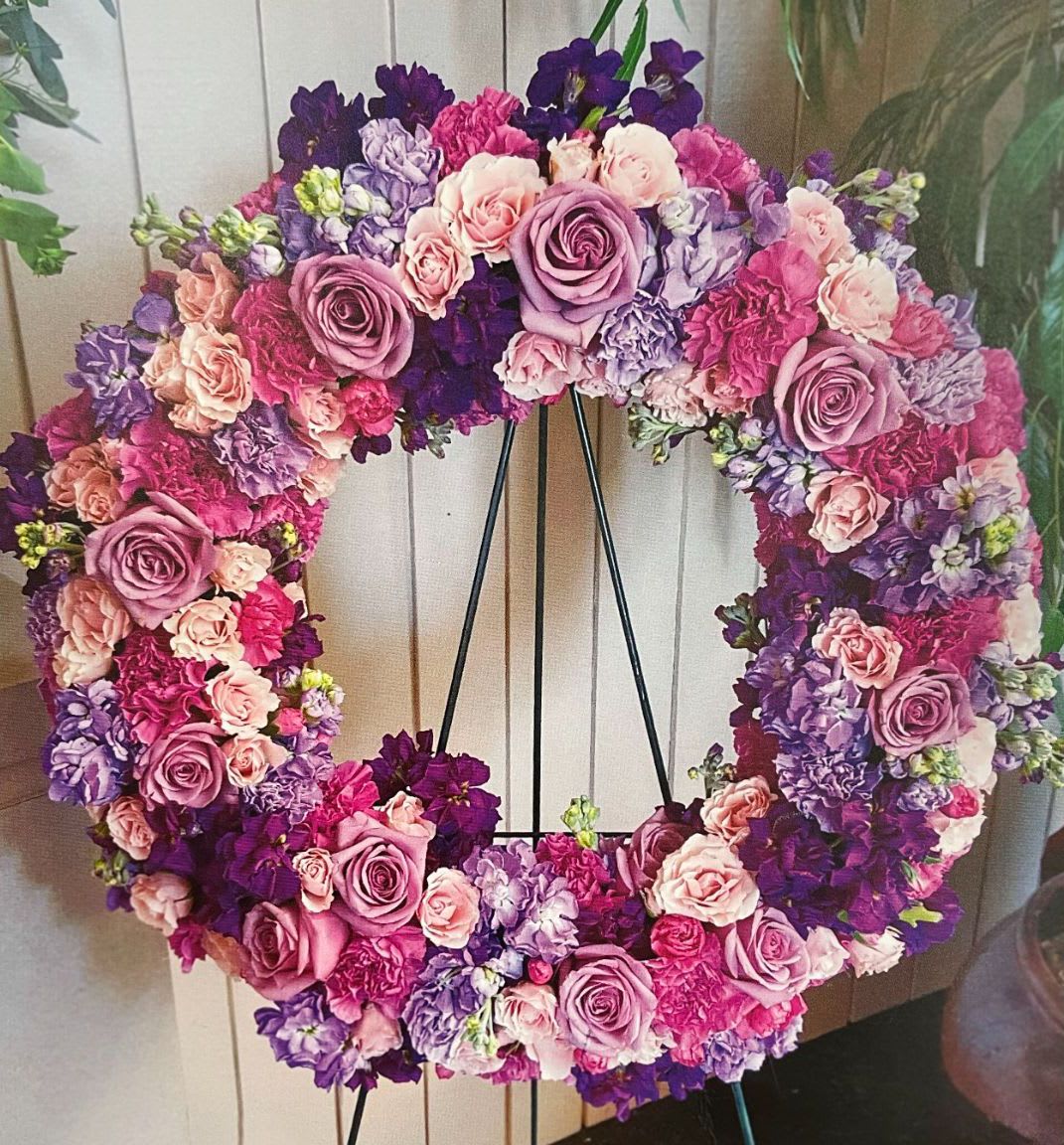 Heart-shaped floral wreath in pink, lavender, and purple blooms on a black stand