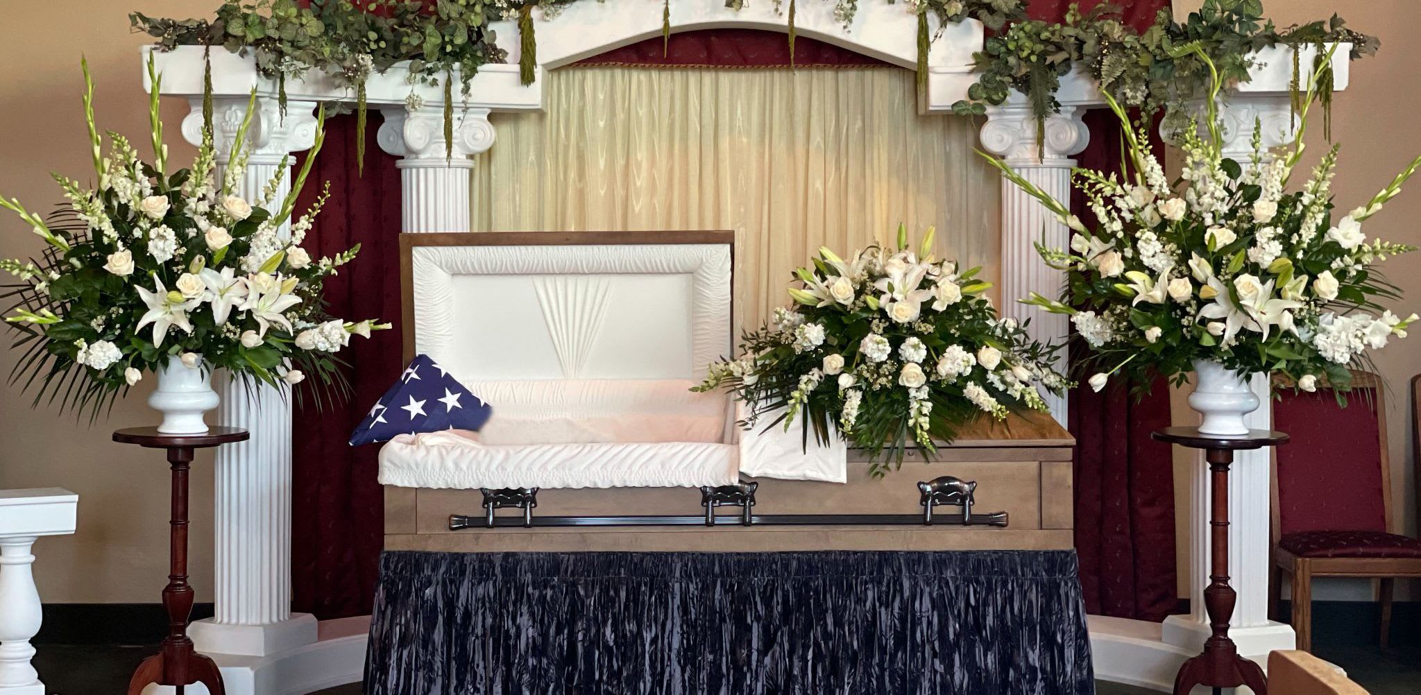 Sympathy casket spray with white lilies and roses beside an open casket