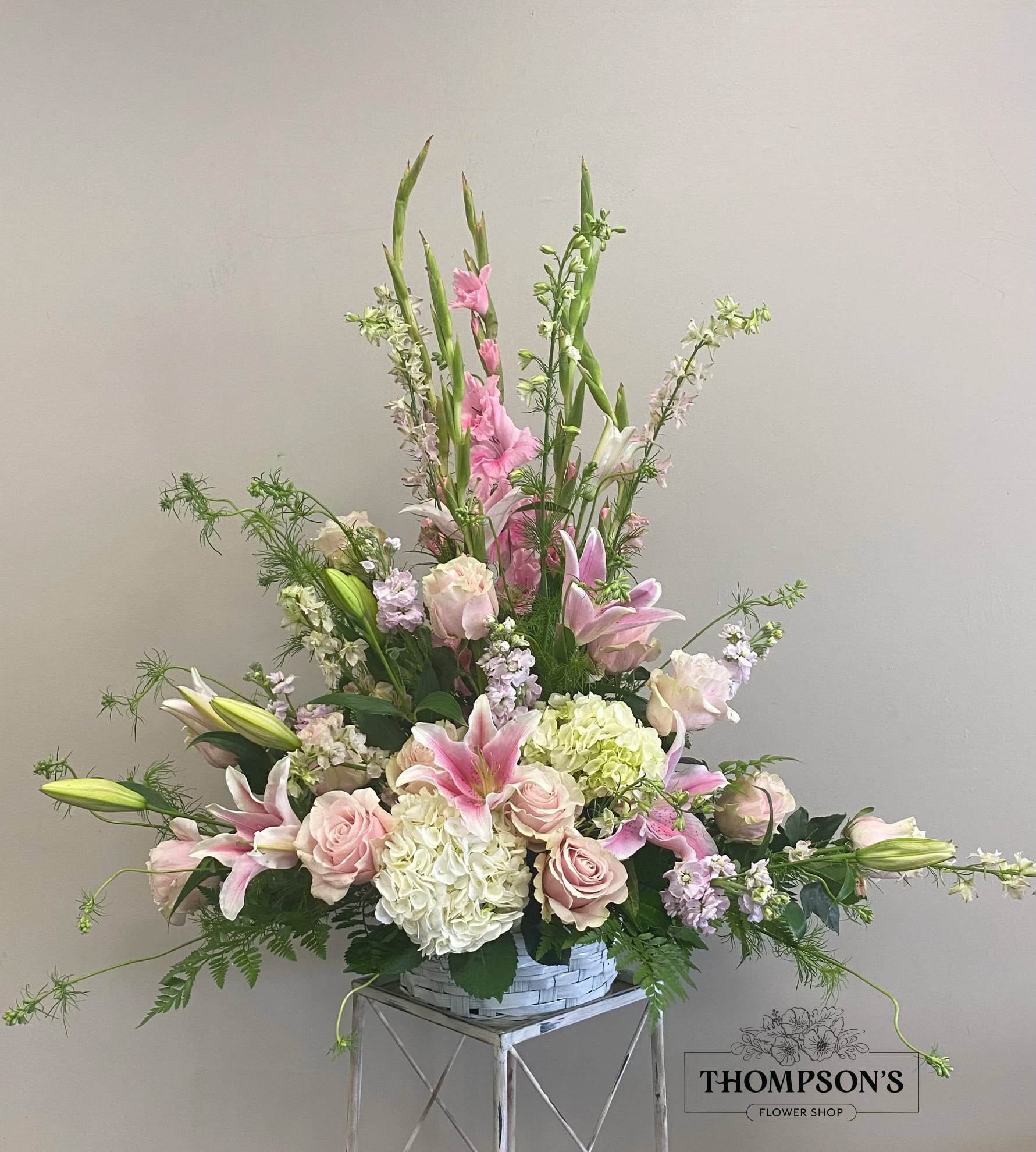 Tall pastel arrangement of pink lilies, roses, and white hydrangeas in a white basket.