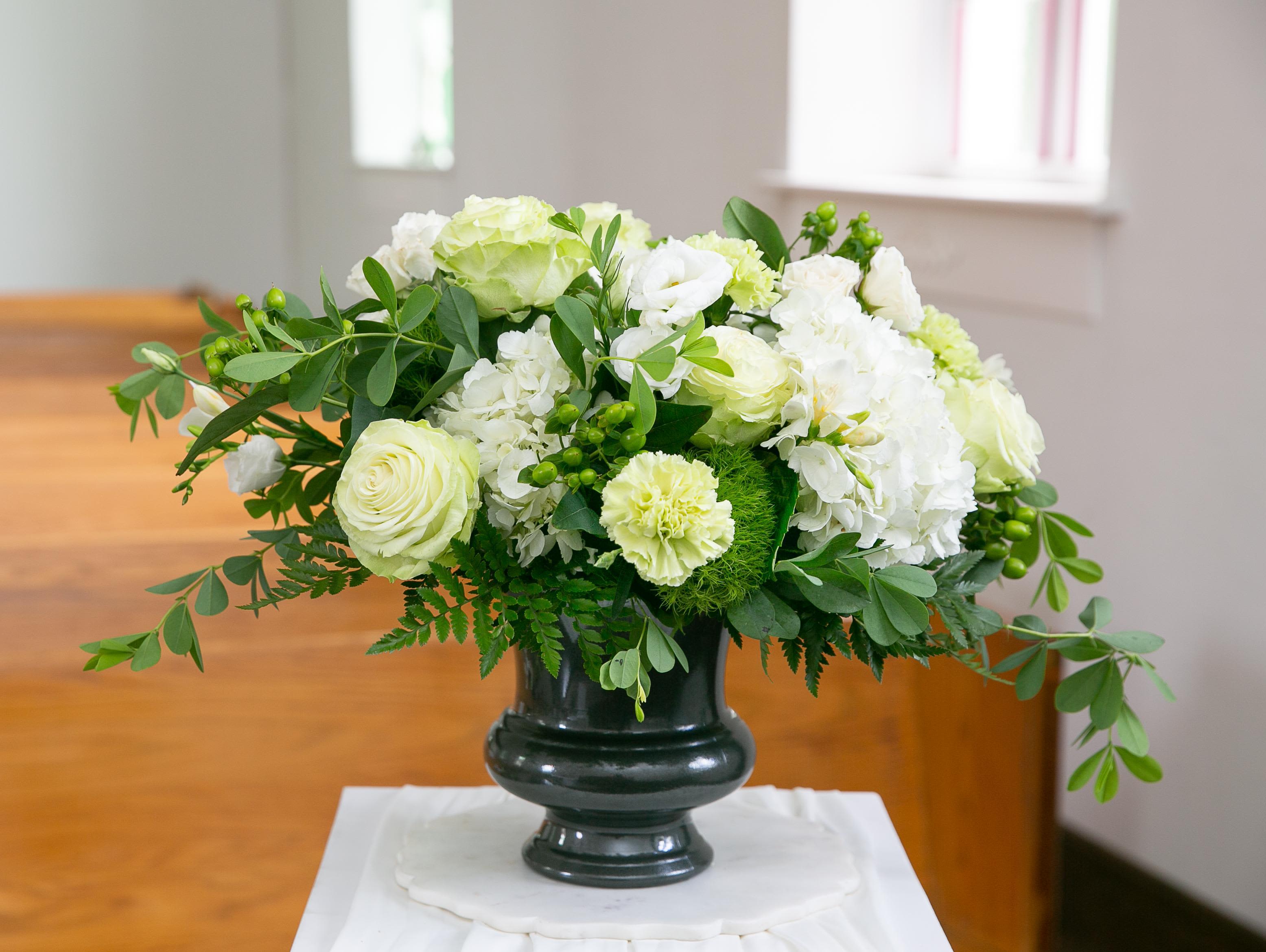 White and pale green floral arrangement in a dark vase