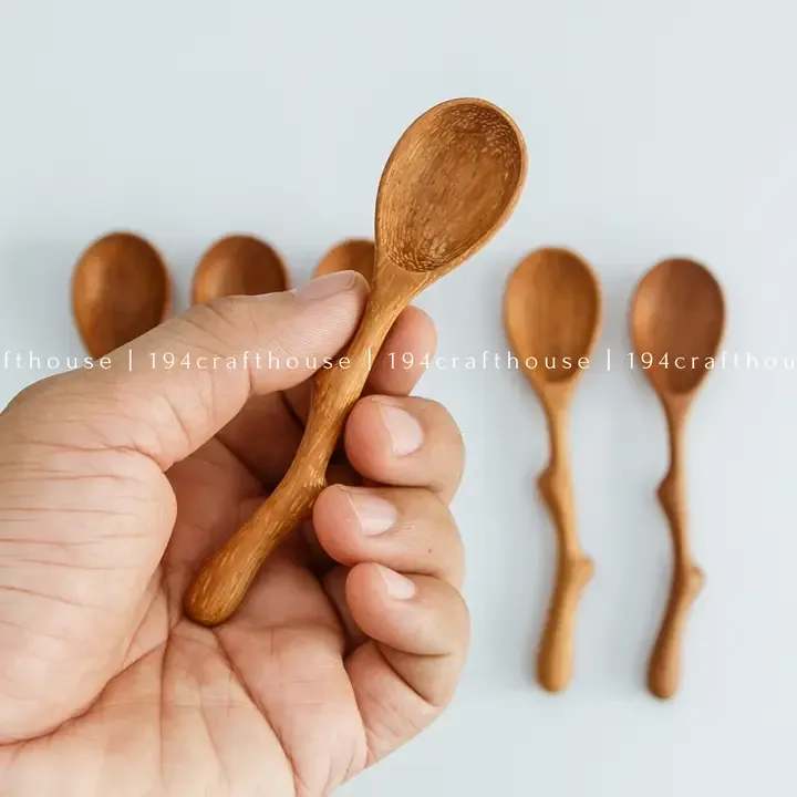 Hand holding a small wooden spoon with more spoons in the background