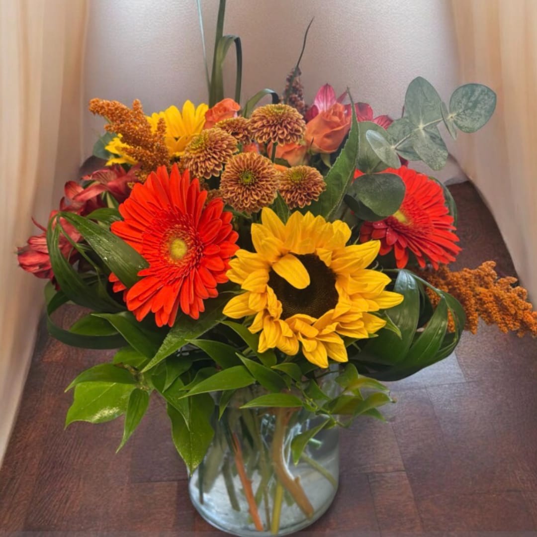 Mixed bouquet of sunflowers, gerbera daisies, and mums in a glass vase