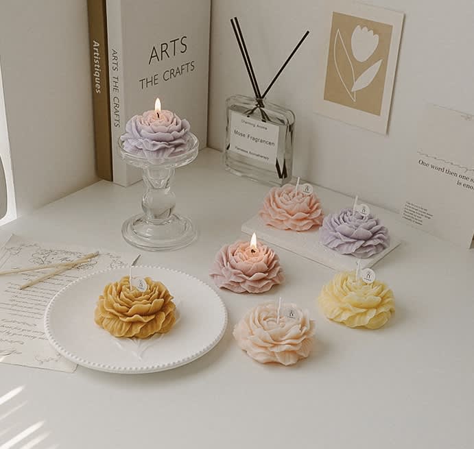 Flower-shaped candles in pastel colors arranged on a white tabletop