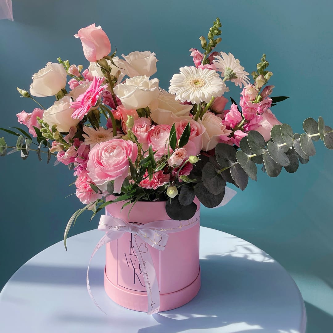 Designers Choice Baby Girl  - Soft pastel blooms arranged in a pink hat box create an immediate, joyful impression-perfect for a baby girl celebration, a birthday, or a tender "thinking of you" moment. The Designers Choice Baby Girl flower arrangement reads feminine and fresh, the kind of gift that makes the person you're thinking of feel genuinely seen: playful, loved, and celebrated. La Rose Flowers London delivers this charming presentation across London, ON for local gifting.  This rounded, abundant design mixes roses, gerbera daisies, carnations, snapdragons, ranunculus and daisy-like blooms in pink, white and green tones, accented with airy eucalyptus-style foliage for a soft silhouette. The arrangement arrives in a pink hat box finished with satin ribbon and ribbon details; photos show styling with a teacup and saucer for a delicate tea-party vibe. Tall stems and a wide spread give it a lush look that sits beautifully on a table or mantel.  Ideal for new baby visits, Mother's Day, birthdays or a cheerful thank-you, this bouquet reads as both celebratory and intimate-a keepsake centerpiece that brightens a room. If you'd like a specific size or delivery timing around a special date, choose your options at checkout so we can prepare and deliver the freshest stems to London, ON when they'll have the most impact.