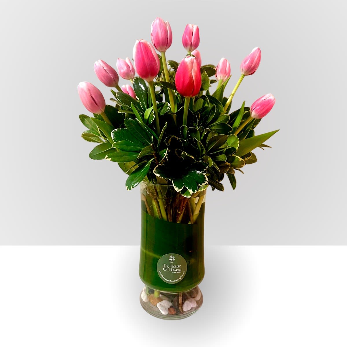 Pink tulips arranged in a tall glass vase with glossy foliage