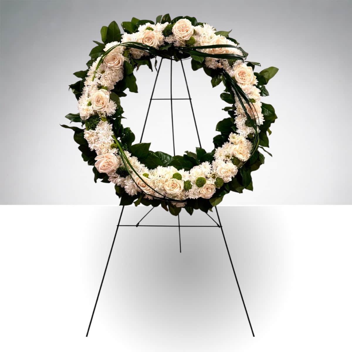 Circular floral wreath of cream roses and white blooms on a black stand