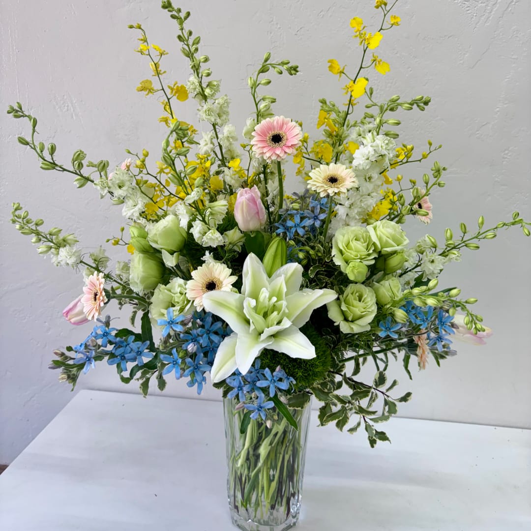 Mixed bouquet in a clear glass vase with lilies, gerberas, and blue flowers