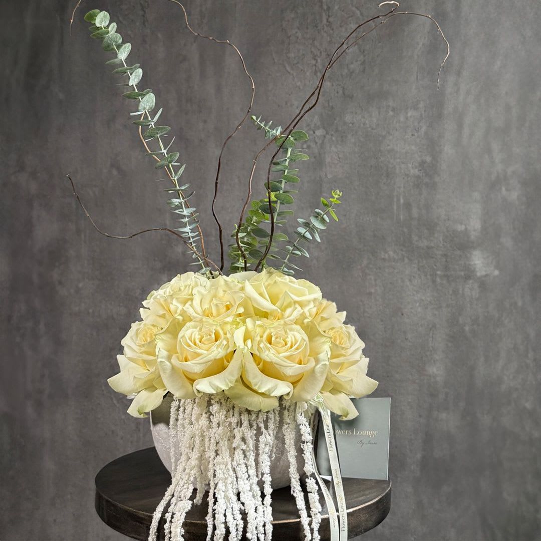 Cream rose arrangement in a round vase with tall eucalyptus branches