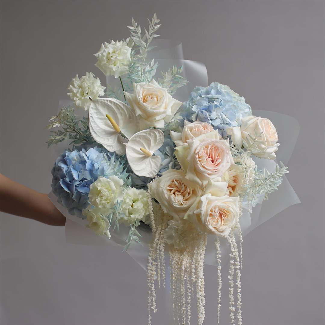 Bouquet of blue hydrangeas, cream roses, and white anthuriums with trailing white accents